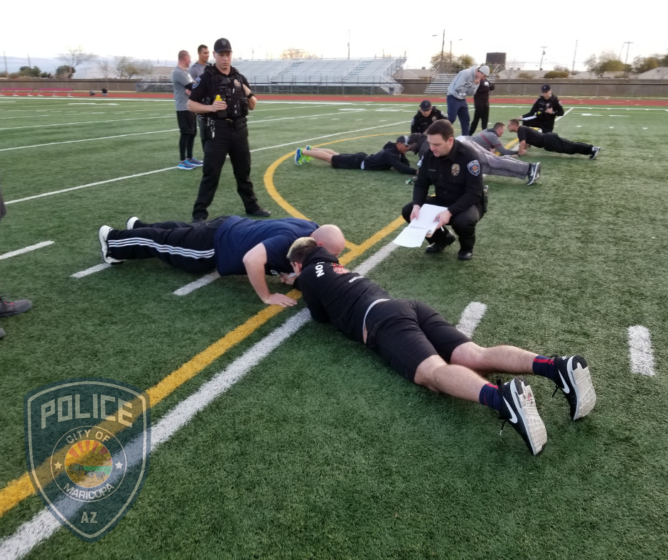 Two applicants doing push-ups on the football field, being observed by officers